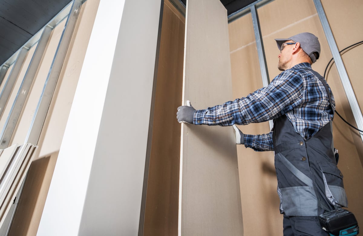 Construction worker fitting a piece of drywall inside a newly built commercial building
