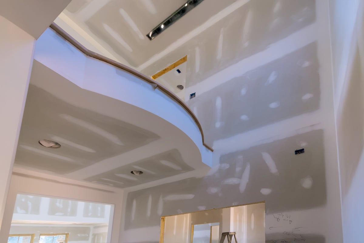 Drywall crew preparing walls in a spacious home with a curved staircase